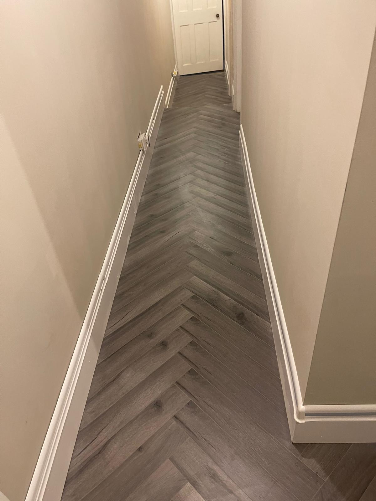 Finished narrow hallway with grey herringbone flooring and fresh trim work