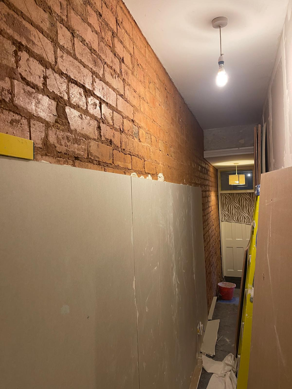 Narrow hallway with exposed brick wall and boards stacked during renovation