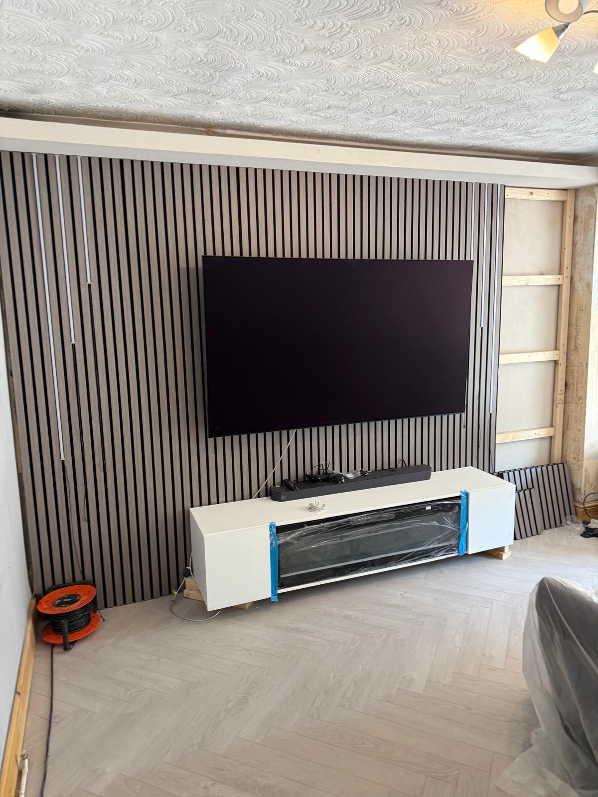Acoustic slat panels part-installed with vertical LED strips and TV mounted