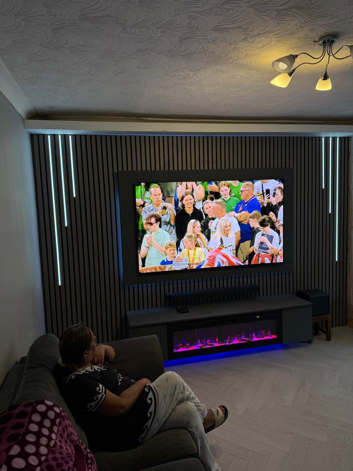 Finished dark slat media wall with LED strips and flame-effect fire lit in the evening